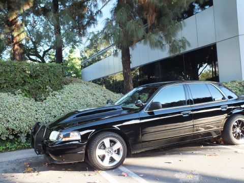 2003 Ford Crown Victoria - Front three-quarter of a black sedan with push bar, dark tint and machined-face wheels in a parking stall.