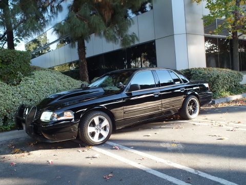 2003 Ford Crown Victoria - Driver-side front-quarter of a lowered black sedan, grille guard up front and tinted windows all around.