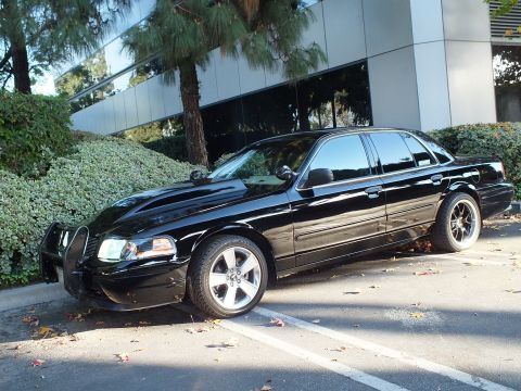 2003 Ford Crown Victoria - Front-quarter view of a black sedan with grille guard and tinted glass parked in a lined office lot.
