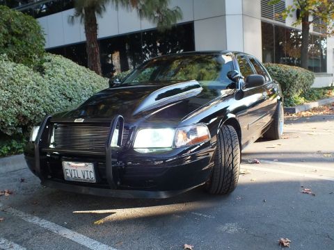 2003 Ford Crown Victoria - Low front-quarter angle of a black sedan, lit headlights, billet grille and EVIL VIC plate behind the push bar.