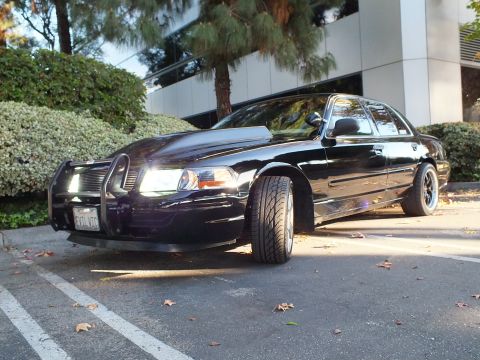 2003 Ford Crown Victoria - Dramatic low front-quarter of a black sedan with push bar, lit headlights and a California vanity plate.