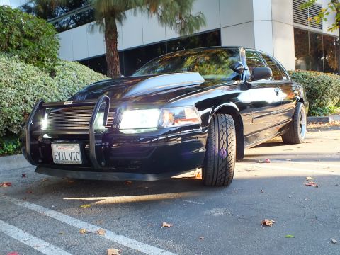 2003 Ford Crown Victoria - Low front-quarter of a black sedan with chrome billet grille, push bar and EVIL VIC California plate.