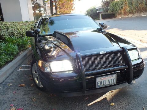 2003 Ford Crown Victoria - Front three-quarter of a glossy black sedan, push bar and billet grille over an EVIL VIC vanity plate.