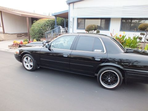 2003 Ford Crown Victoria - Driver-side profile of a black full-size sedan on dark wheels, parked along a building marked 535.