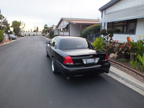 2003 Ford Crown Victoria - Rear-quarter view of a black sedan, Ford oval on the trunk, parked along a quiet residential street.