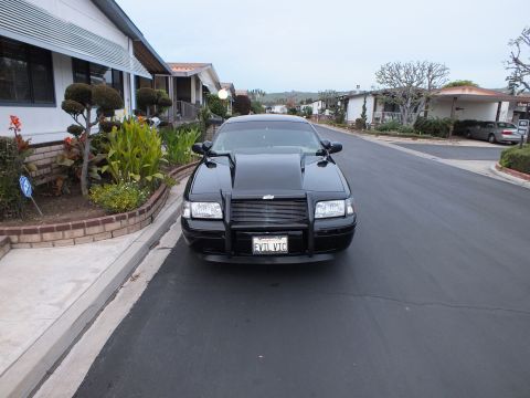 2003 Ford Crown Victoria - Direct front angle showing the grille guard and dual hood ridges of a black Crown Victoria sedan.