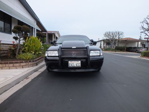 2003 Ford Crown Victoria - Low front-on view of a black Crown Victoria with chrome push bar against a single-story home.