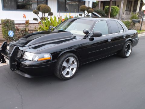 2003 Ford Crown Victoria - Driver-side front three-quarter of a black Crown Victoria with push bar and dark spoke wheels.