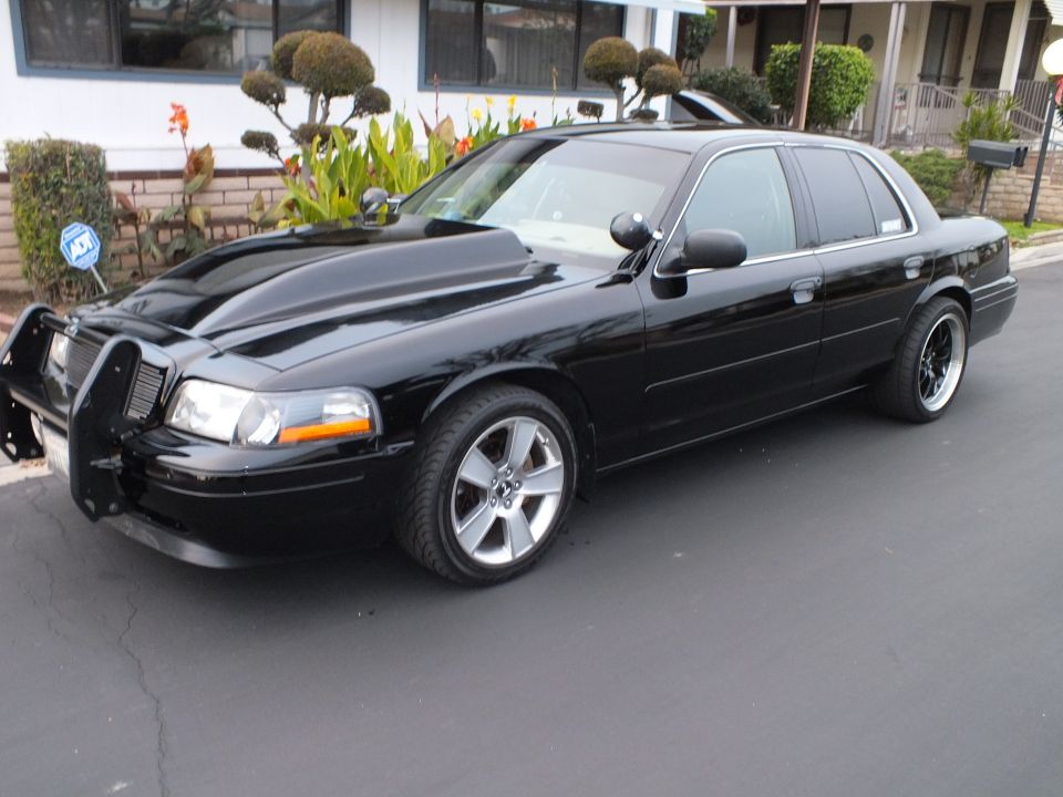 Black Ford Crown Victoria driver-side front three-quarter on driveway with black alloy wheels