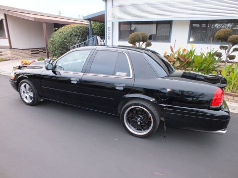 2003 Ford Crown Victoria - Rear-quarter driver-side view of a black Crown Victoria with trunk spoiler and black alloys.