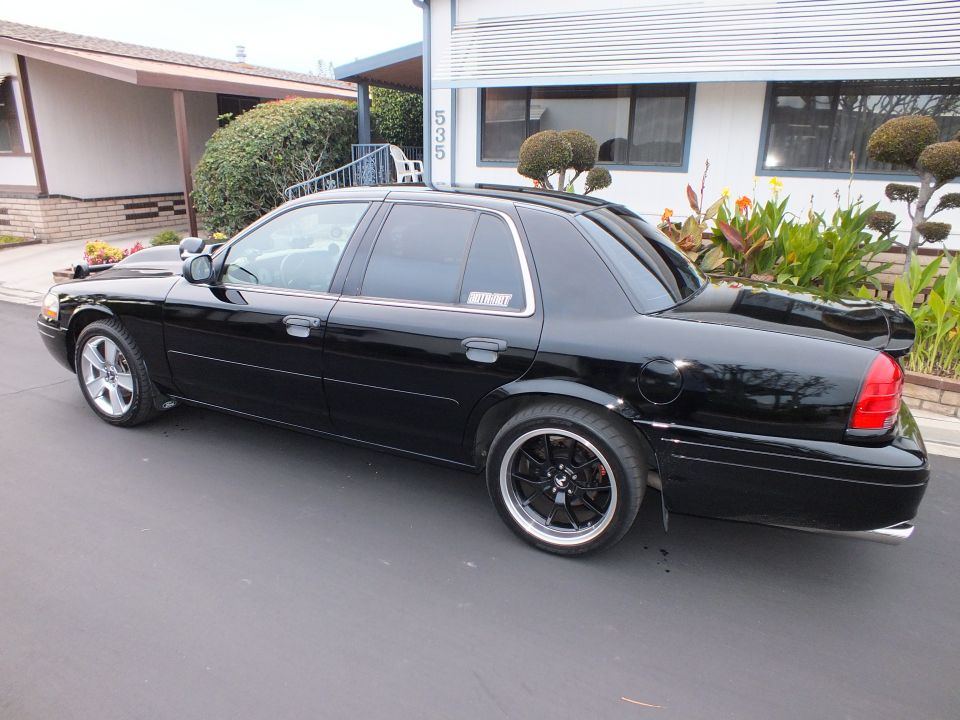 Black Crown Victoria rear three-quarter driver side with deck spoiler and black wheels