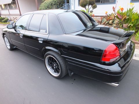 2003 Ford Crown Victoria - Driver-side rear quarter of a black Crown Victoria showing tail light, spoiler and rocker trim.