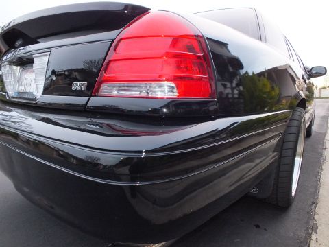 2003 Ford Crown Victoria - Close-up of the right taillight on a black Crown Victoria showing an SVT badge below clear and red lenses.