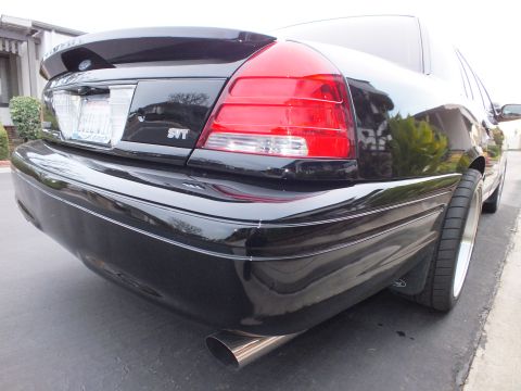 2003 Ford Crown Victoria - Rear bumper corner of a black Crown Victoria with SVT taillight badge and an angled polished exhaust tip below.