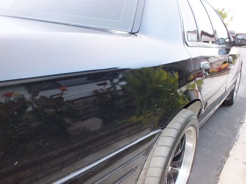 2003 Ford Crown Victoria - Glossy black sedan flank with reflections of foliage across the rear door and a polished-lip rear wheel.