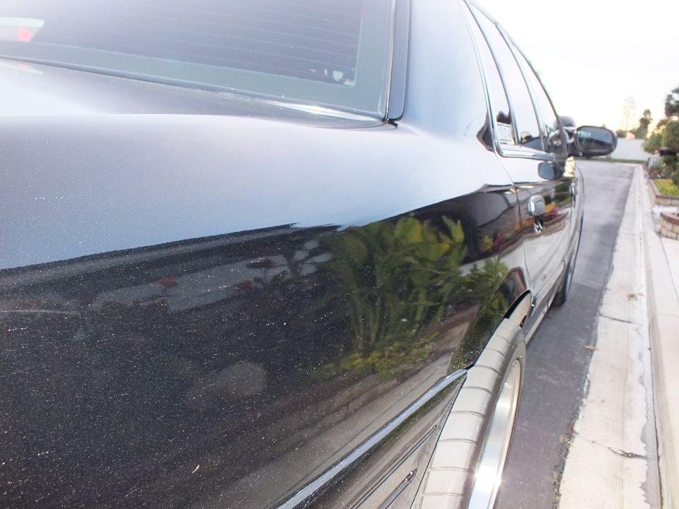 Black sedan rear quarter panel and door with mirror reflection of foliage