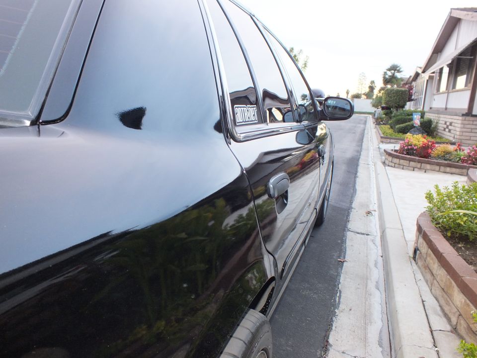 Black sedan front door and side mirror at curb with landscaped yard behind