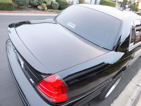 2003 Ford Crown Victoria - Overhead angle across a black sedan trunk lid and backlight down to the red taillight and polished wheel.