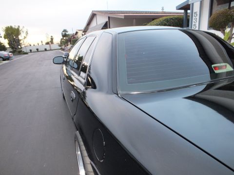 2003 Ford Crown Victoria - Tinted rear window and roof of a black sedan at the curb, a house marked 535 in the background.