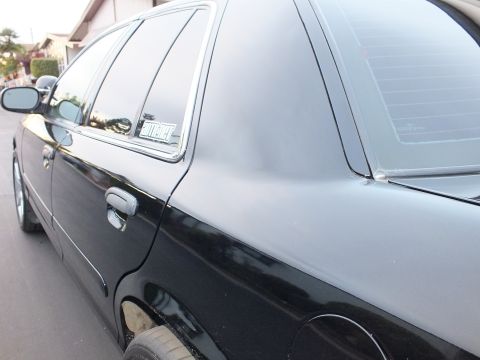 2003 Ford Crown Victoria - Black sedan rear door and quarter window with a small decal, chrome handle and dark wheel below.