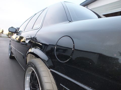 2003 Ford Crown Victoria - Rear quarter of a black sedan showing the round fuel door and a polished-lip wheel with low-profile tire.