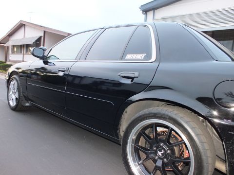 2003 Ford Crown Victoria - Full side profile of a black sedan on dark mesh wheels with a quarter-window decal and folded mirror.