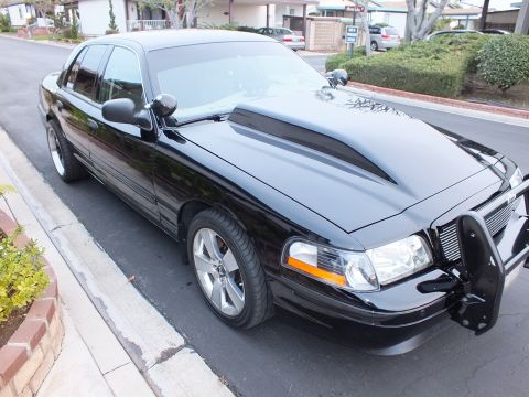 2003 Ford Crown Victoria - Front three-quarter of a black Crown Victoria fitted with a tubular push bar over a black mesh grille.