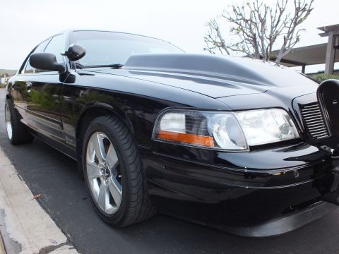 2003 Ford Crown Victoria - Front corner of a black Crown Victoria showing headlight, amber marker, black grille and a machined-face wheel.