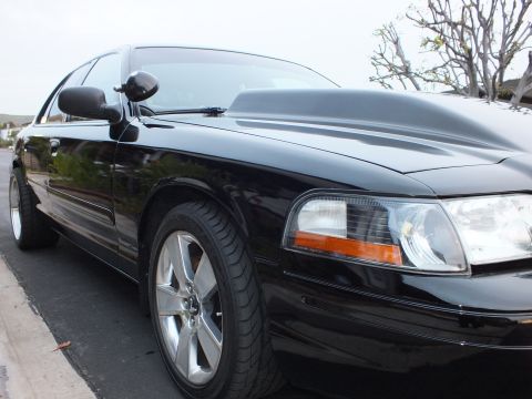 2003 Ford Crown Victoria - Low front three-quarter of a black Crown Victoria with reflective hood, clear headlight and machined wheel.