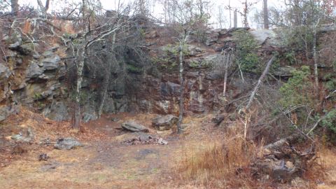 1986 Ford Bronco - A natural scene of a rocky cliff face and surrounding dry vegetation, with a fire pit in the clearing.