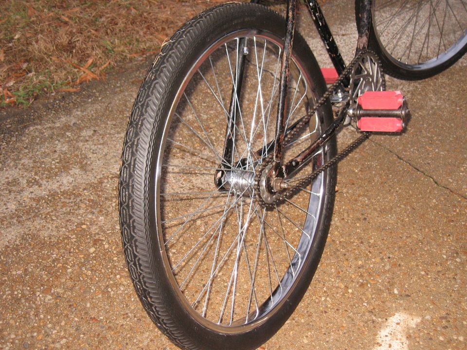 close up of bicycle rear wheel, chain, and red pedals