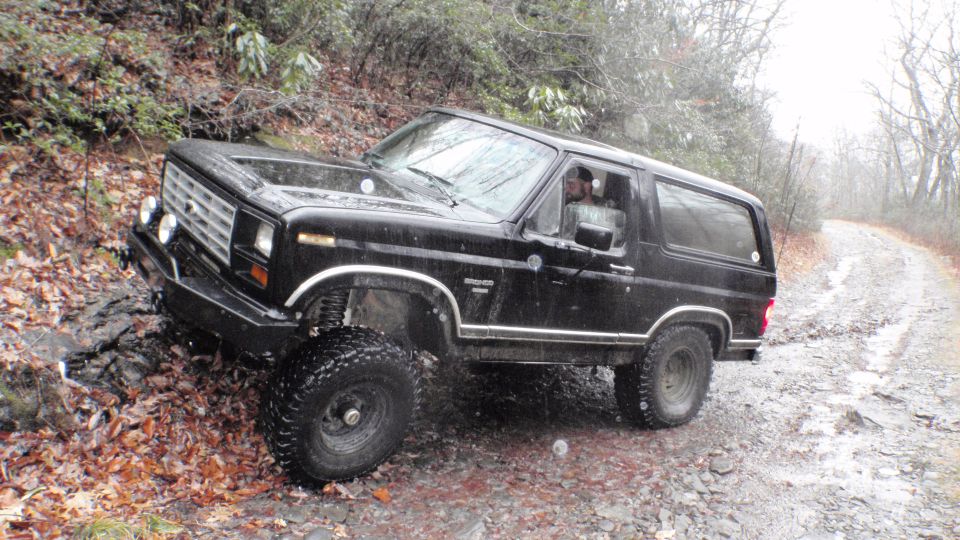 Black Ford Bronco with lifted suspension and off-road tires navigating a wet, wooded trail