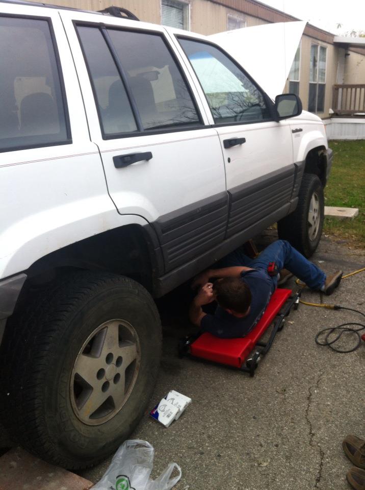 White SUV side view, person working underneath on creeper