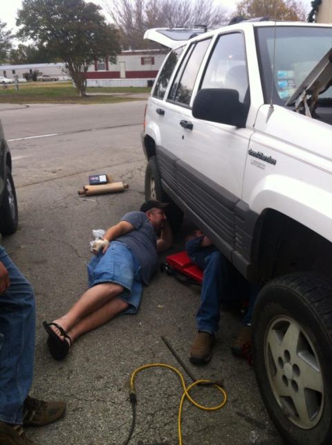 1989 Ford Bronco - Mechanics are performing maintenance on a white Jeep Grand Cherokee, with the hood and rear hatch open.