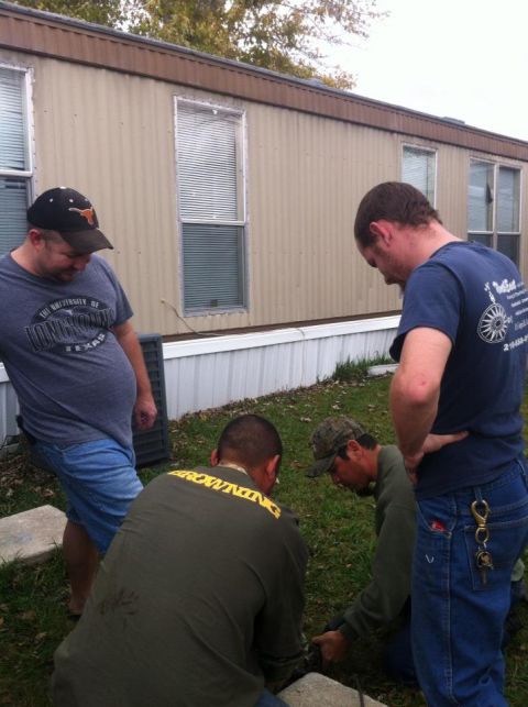 1989 Ford Bronco - A group of men are focused on an object on the ground outside a mobile home.