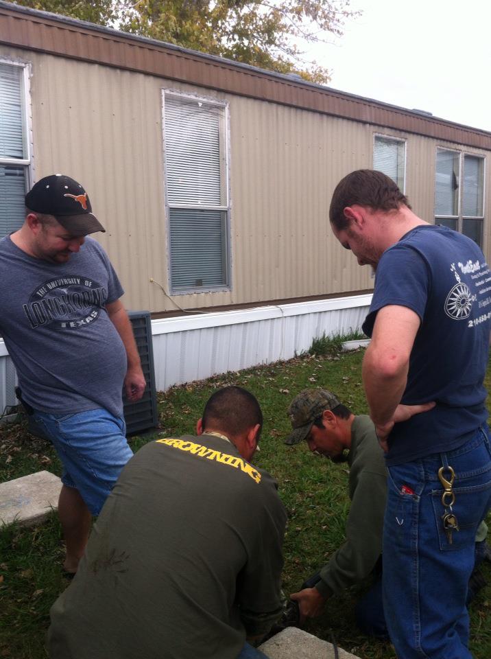 Four men gathered around something on the ground in front of a mobile home