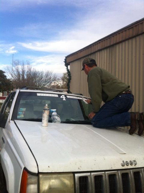 1989 Ford Bronco - A person cleans the windshield of a white Jeep Grand Cherokee, which has a "WEEKEND 4 WHEELER" sticker.