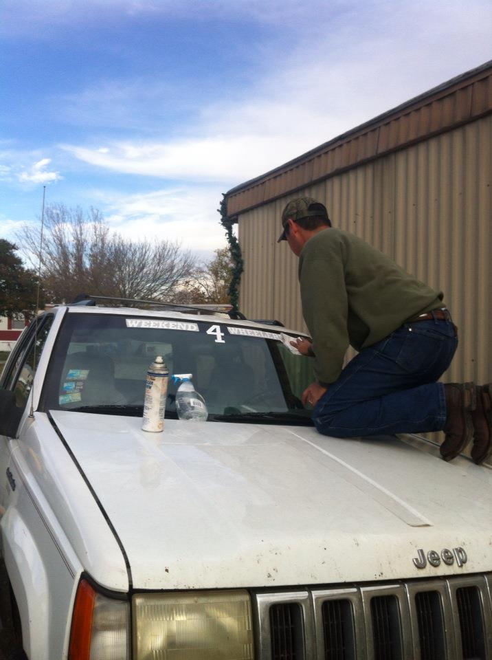 Guy cleaning windshield of a white Jeep Grand Cherokee. "WEEKEND 4 WHEELER" sticker on windshield