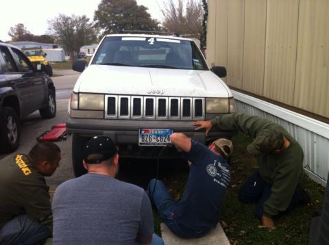 1989 Ford Bronco - Several individuals are gathered around the front of a white Jeep Grand Cherokee, appearing to work on the vehicle.