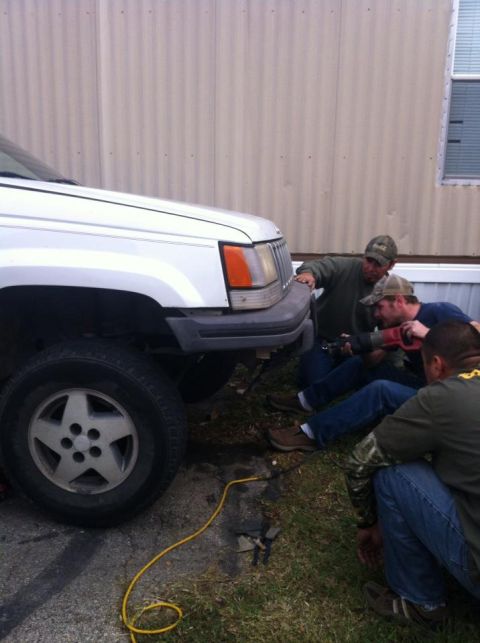 1989 Ford Bronco - Three men work on the front bumper of a white Jeep Grand Cherokee.