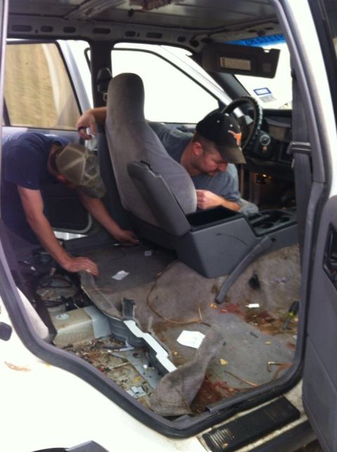 1989 Ford Bronco - Two individuals are seen working on the interior of a vehicle, with seats and floor components exposed.