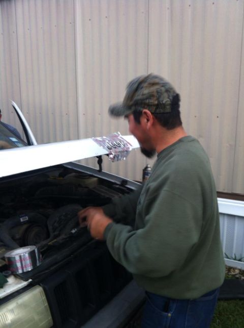 1989 Ford Bronco - Man works on car engine under an open hood, with duct tape visible on the side.