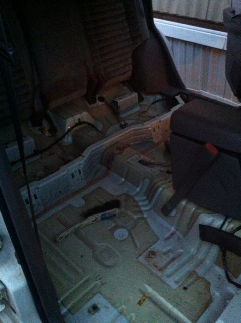 1989 Ford Bronco - The interior of a vehicle is shown with the seats removed, revealing a dirty floor and exposed metal components.