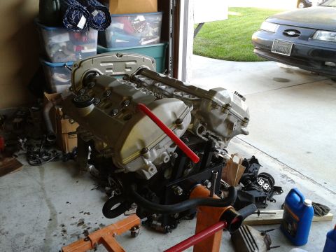 1992 Ford Taurus - Engine on a stand in a garage, with a dark sedan parked outside.