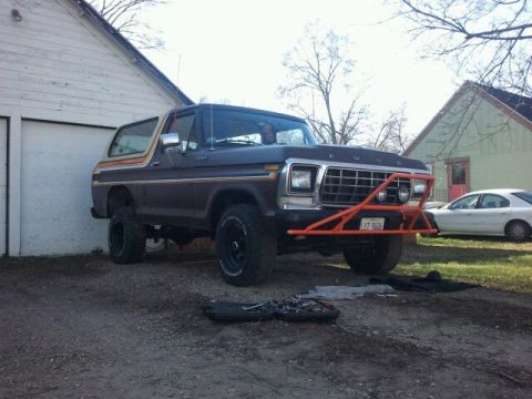 1979 Ford Bronco - A dark brown Ford Bronco with an aftermarket orange brush guard is parked in a driveway next to a garage.