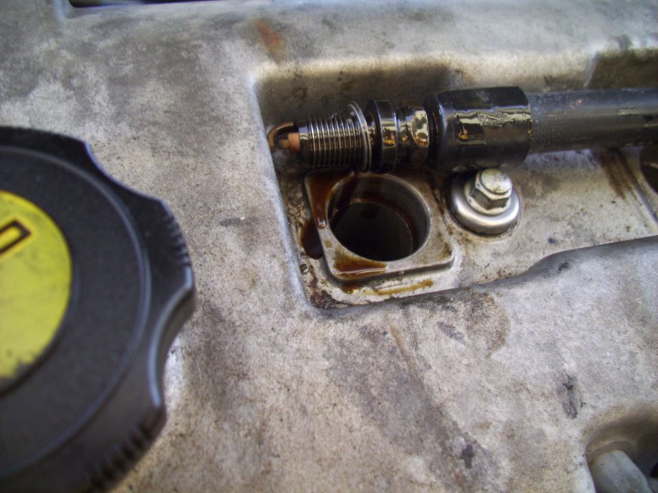 Spark plug removed from engine valve cover with oil residue
