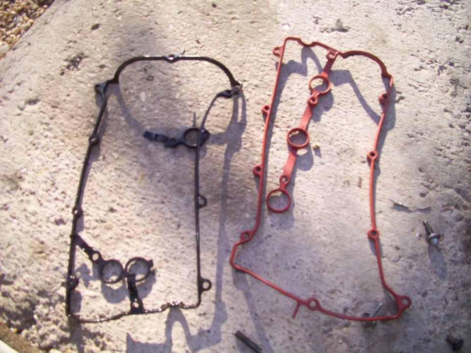 two valve cover gaskets, one black and one red, lying on concrete