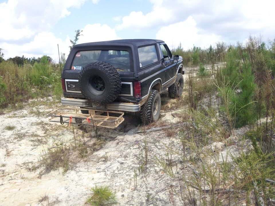 Black 1986 Ford Bronco with spare tire on rear, off-road tires, and cargo rack on uneven terrain
