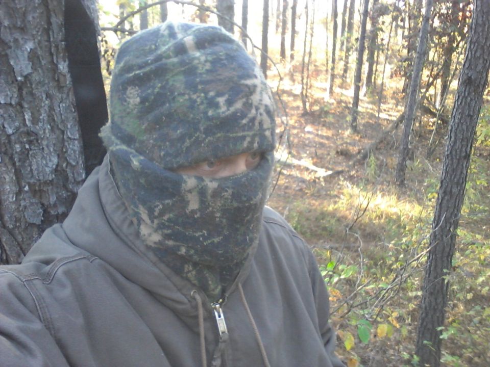 Person wearing camouflage hat and face covering in a wooded area