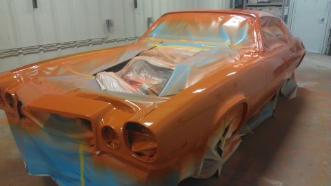 1973 Chevrolet Camaro - A car is being painted orange, with its engine bay and interior covered for protection.